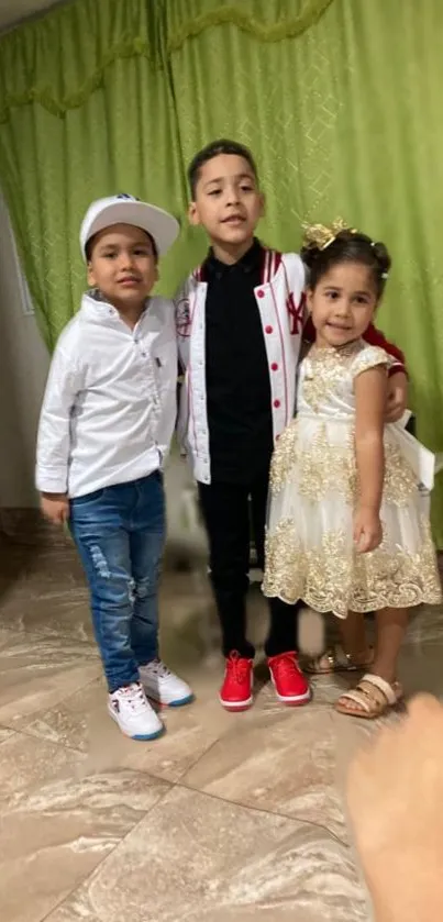 Three children posing indoors in colorful outfits with a green background.