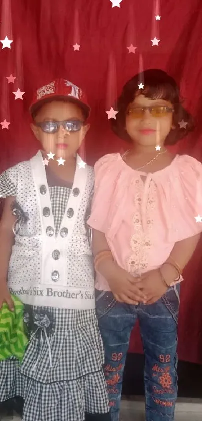 Two stylish kids posing with a red backdrop.