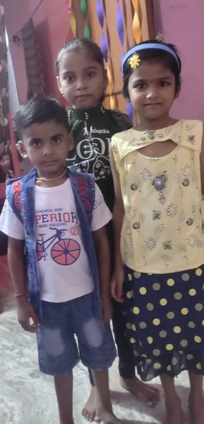 Three children in colorful outfits standing indoors, smiling at the camera.