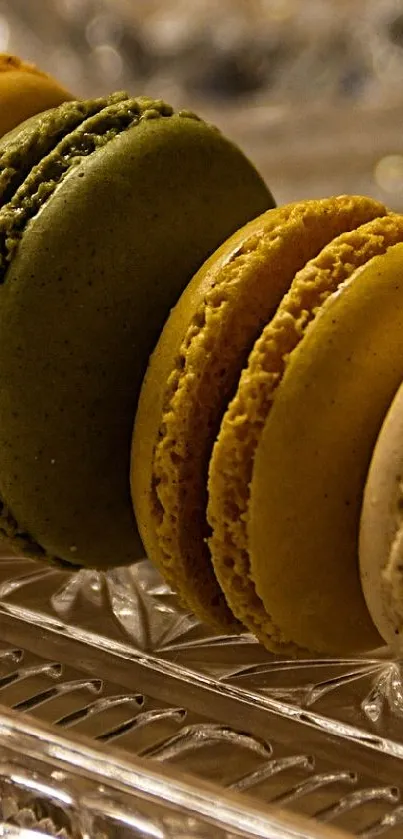 A row of colorful macarons displayed on an elegant glass tray with a beige background.