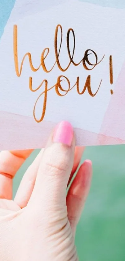 Hand holding a colorful 'Hello You' card over turquoise ocean.