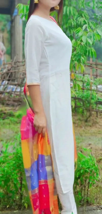 Person in white outfit with colorful scarf in a green outdoor setting.