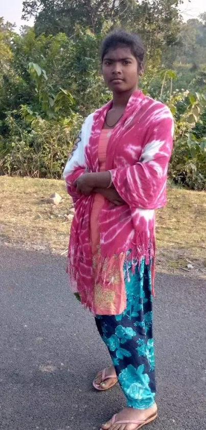 Woman standing outdoors in colorful attire with nature background.