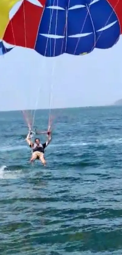 Person parasailing over blue ocean with colorful parachute.