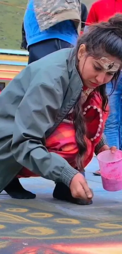 Woman creating colorful rangoli design on pavement with pastel colors.