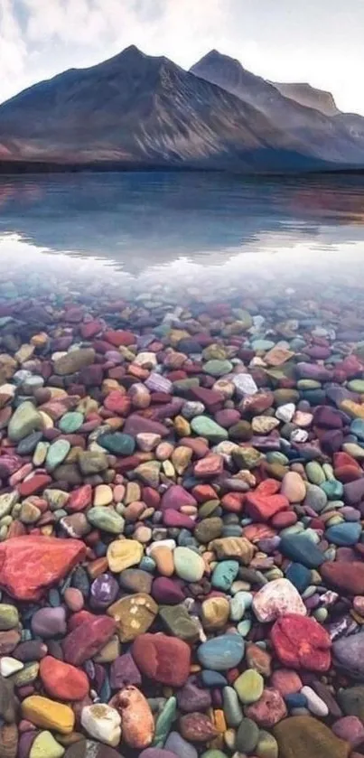 Colorful stones under clear water with mountain reflection.