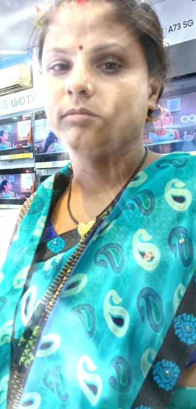 Woman in blue-green saree in a store setting, colorful wallpaper.