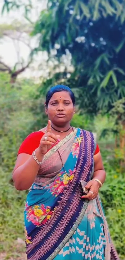 Woman in a colorful saree standing outdoors amidst lush greenery.