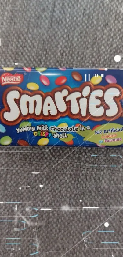 Smarties candy box on gray fabric background, showcasing colorful candies.