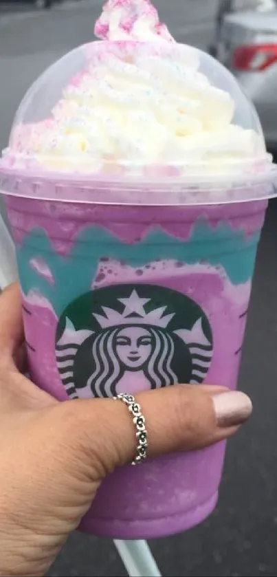 Hand holding a pink and blue unicorn frappuccino from Starbucks.