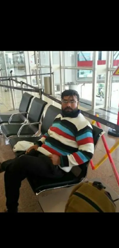 Person in colorful striped sweater sitting in airport.