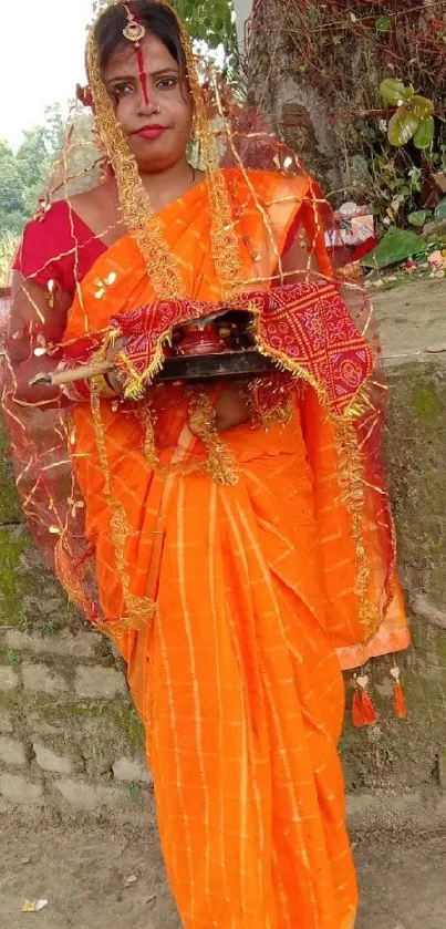 Woman in vibrant orange sari stands gracefully by a historic wall.