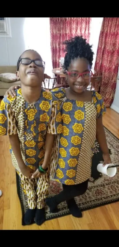 Two smiling children in colorful, traditional attire indoors.