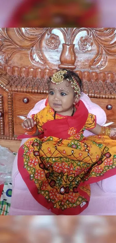 Baby in colorful traditional attire sitting on a wooden carved chair.