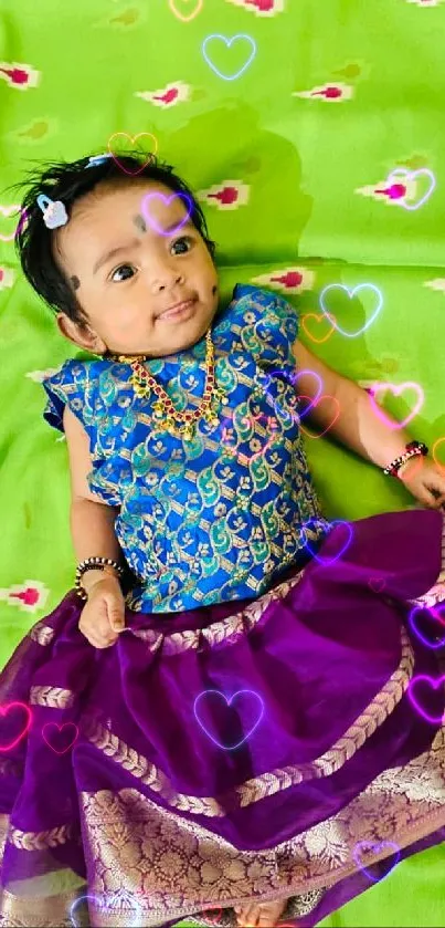 Smiling baby in colorful traditional Indian outfit on green background.