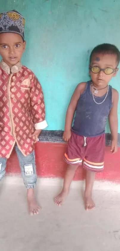 Two kids in colorful attire stand against a multicolored wall.