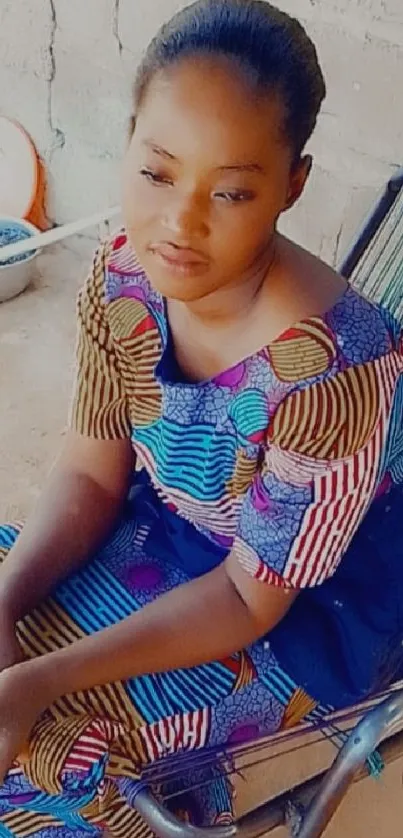 Woman in colorful traditional dress sitting on a chair in natural light.