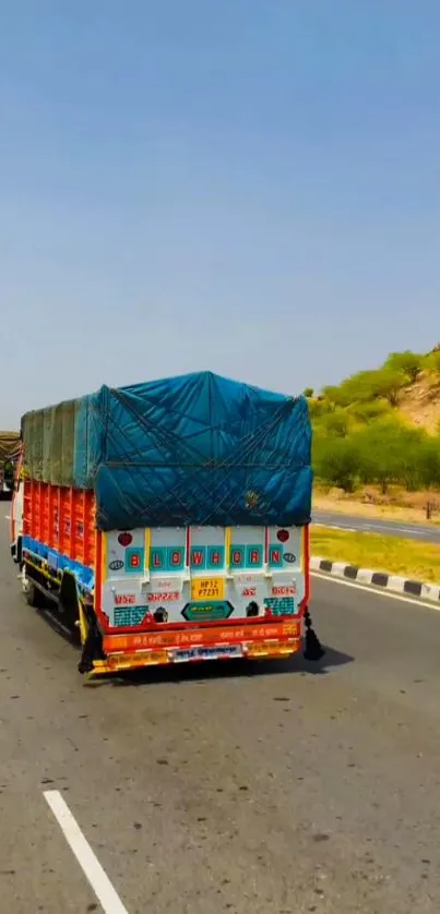 Colorful Indian truck driving on scenic highway with blue sky.