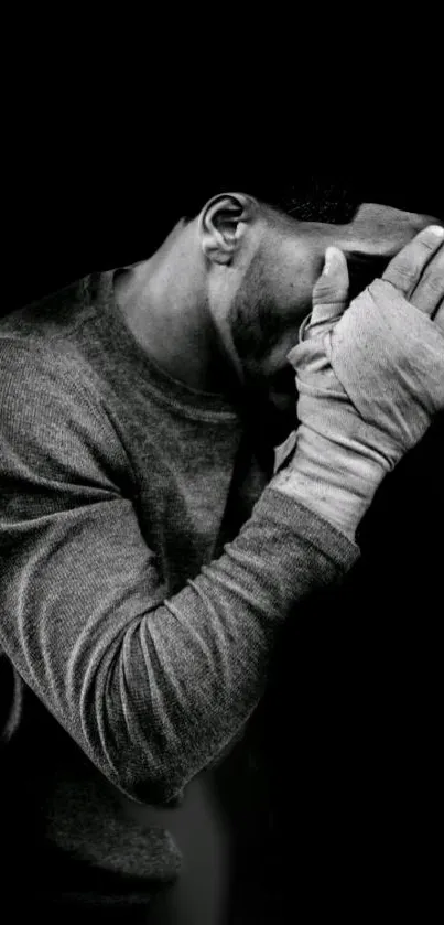 Monochrome image of a contemplative boxer with wrapped hands against a black background.