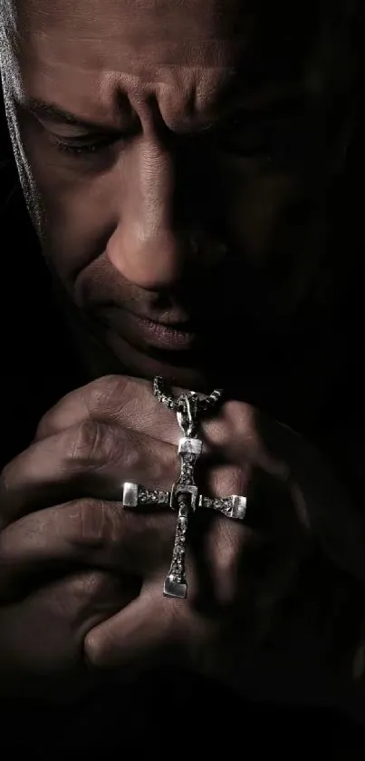 Man holding a cross in a contemplative mood, dark background.