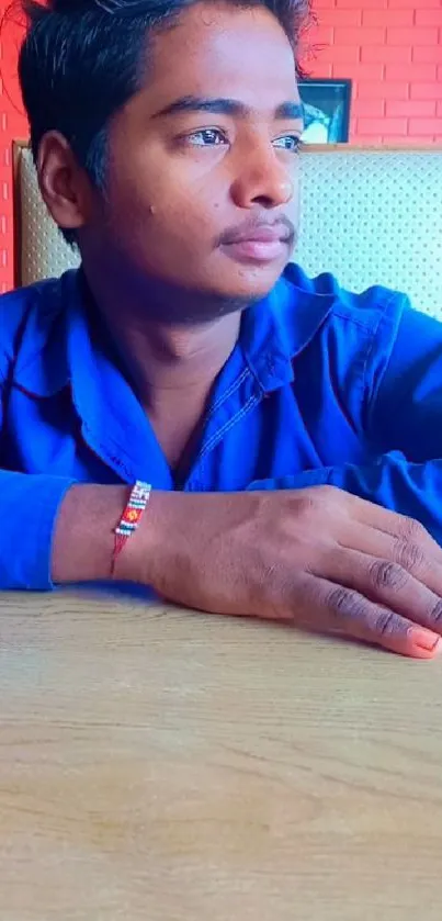 Person in blue shirt sitting thoughtfully against a red brick wall.