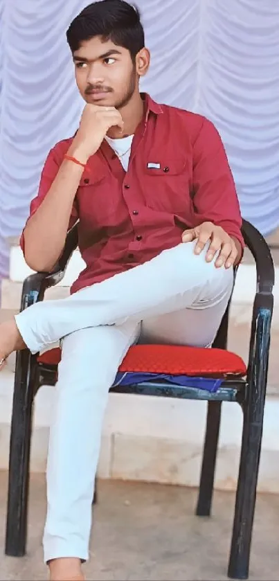 Young individual in red shirt sitting thoughtfully on chair.