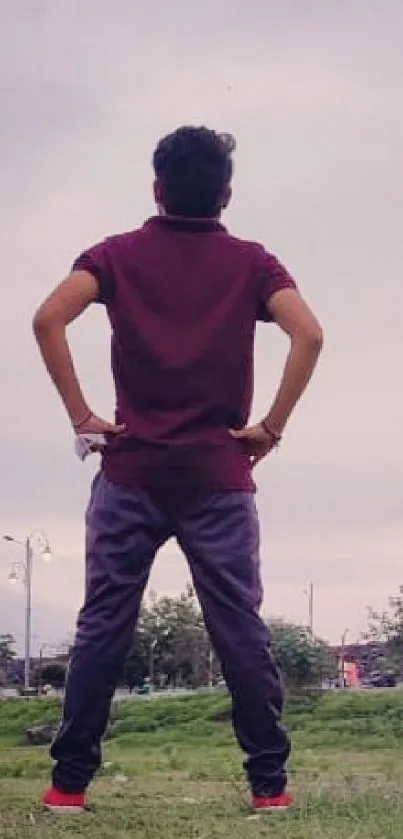 Person stands thoughtfully in urban landscape with sky backdrop.