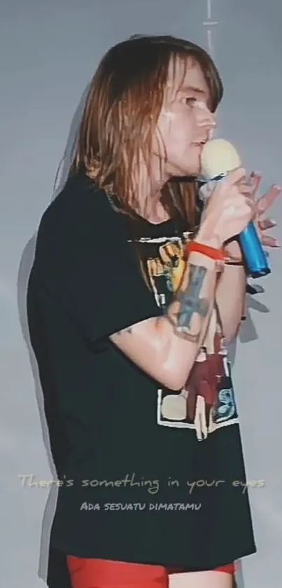 Performer singing on stage with a blue microphone and gray backdrop.