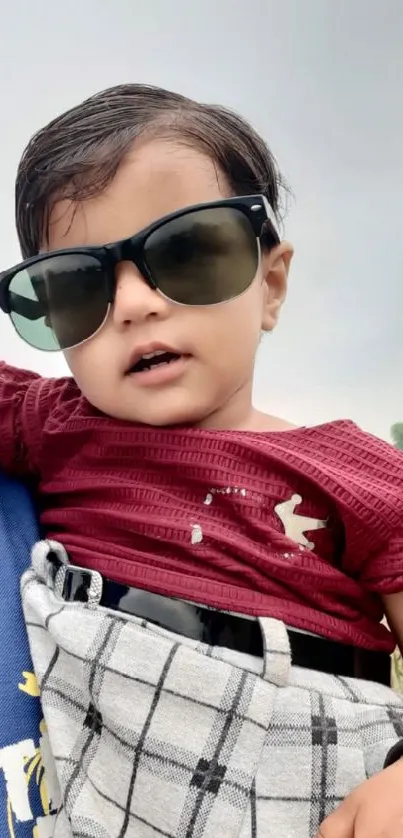 Adorable baby in sunglasses with burgundy shirt.