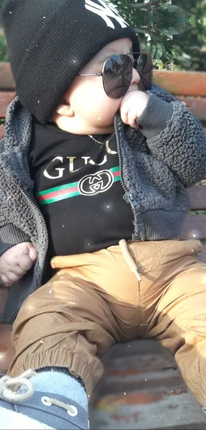 Cute baby in trendy outfit with sunglasses on a bench.