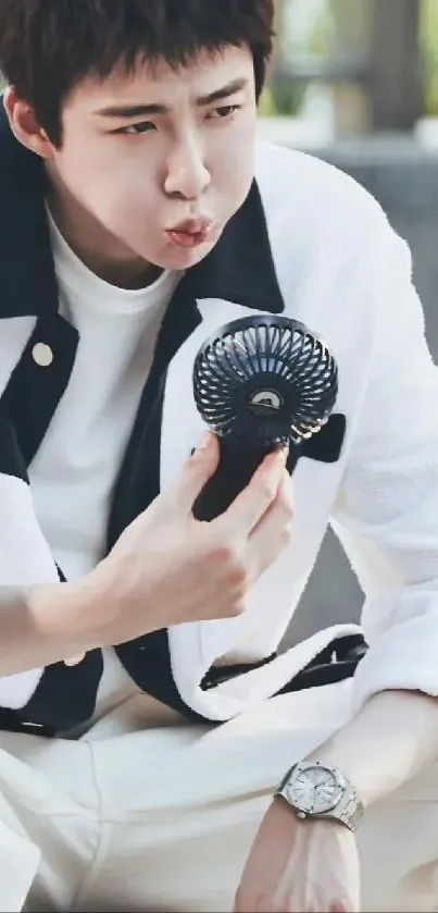 A young person in stylish casual wear holding a small fan.