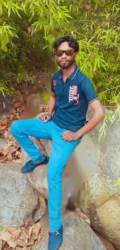 Stylish man sitting on rocks surrounded by lush green foliage.