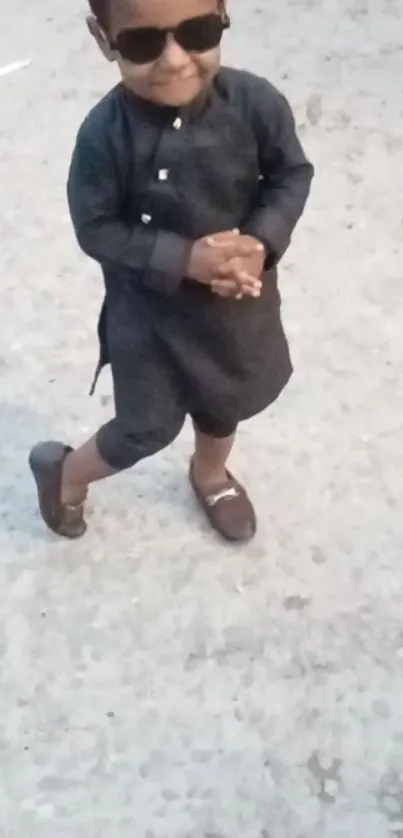 Child in black outfit with sunglasses on a gray pavement.