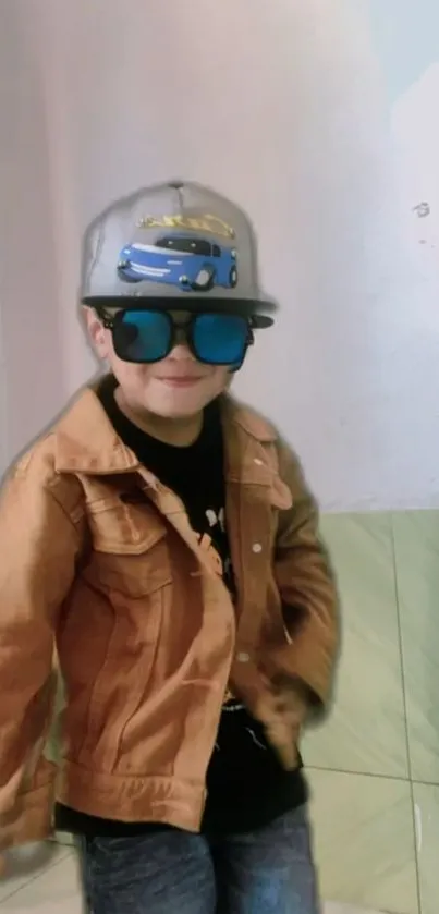 Young boy in a brown jacket, sunglasses, and a hat with a car design.