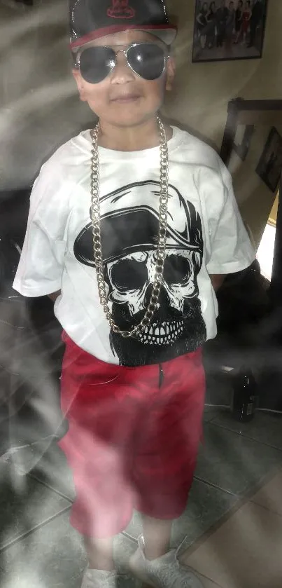 Kid in sunglasses wearing skull t-shirt and red shorts with a gold chain.