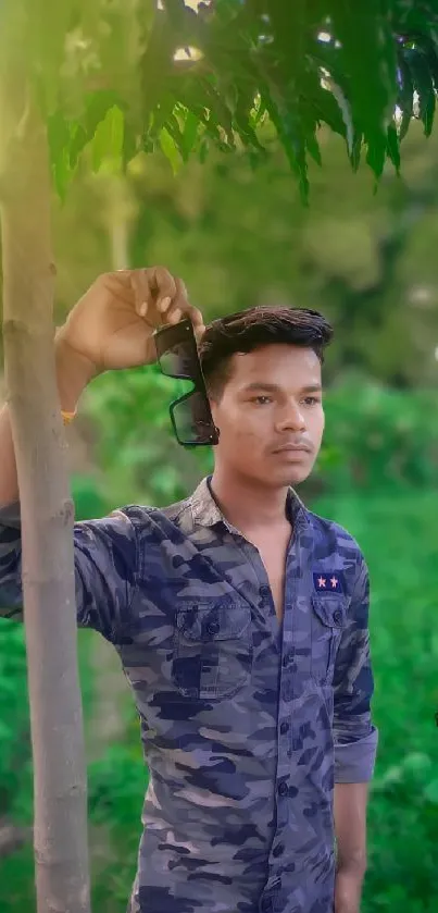 A young man poses outdoors amidst green foliage and natural sunlight.