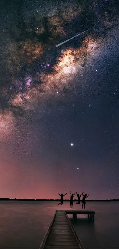 Friends silhouetted against Milky Way over a peaceful lake at night.