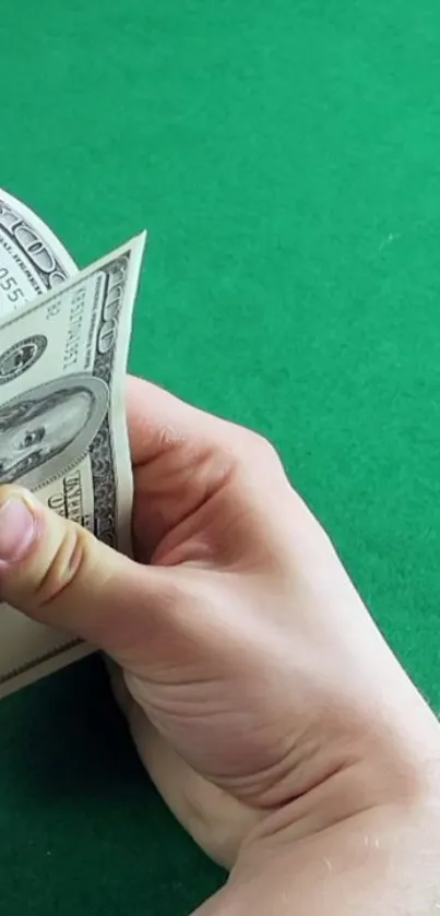 A hand counts hundred-dollar bills on a vibrant green surface.