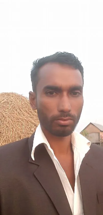 Man in a suit with rural haystack backdrop, daytime setting.