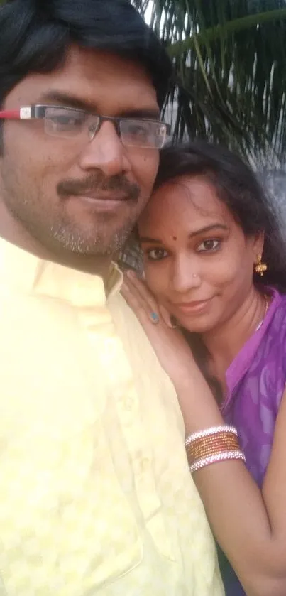 A couple in colorful attire hugging outdoors with leafy backdrop.