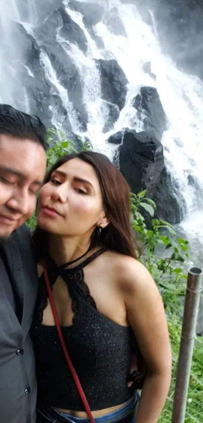 A couple standing before a majestic waterfall surrounded by lush greenery.