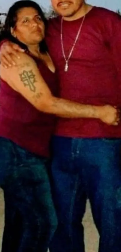 Couple standing together in matching maroon tops and blue jeans.