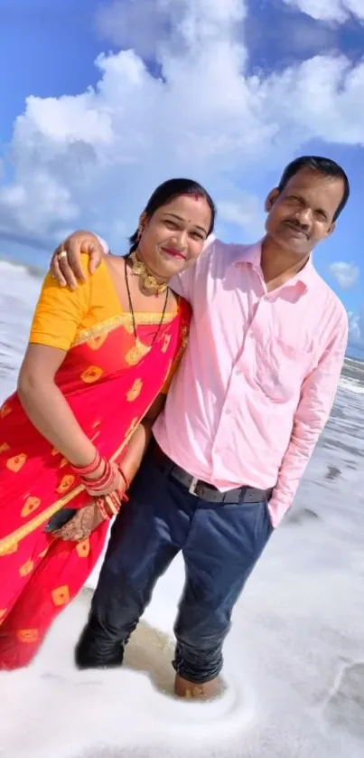 Couple standing on a scenic beach with waves and blue skies.