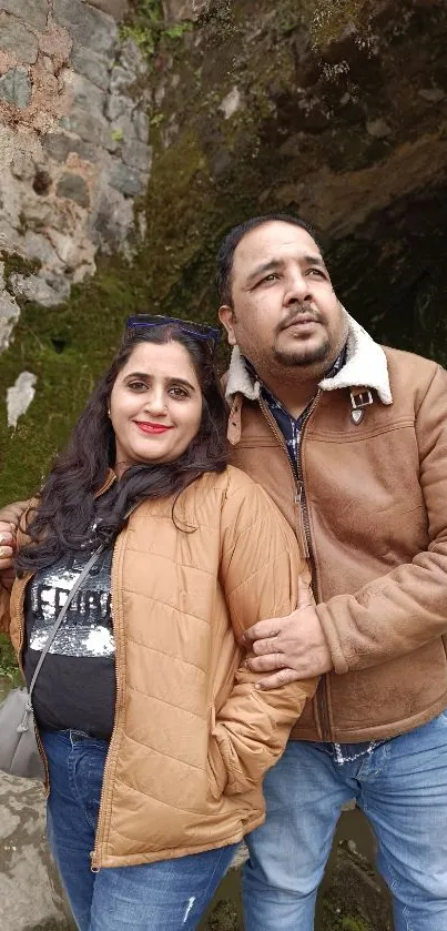 A couple in brown jackets embracing outdoors, showcasing a natural backdrop.