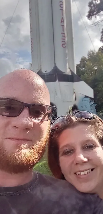 Couple taking a selfie with a large rocket in the background.