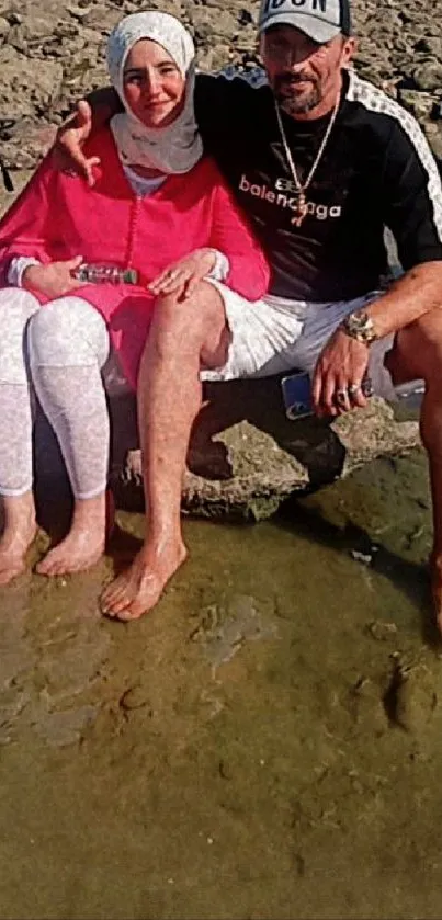 A couple sitting on rocks by the beach, enjoying the sun.