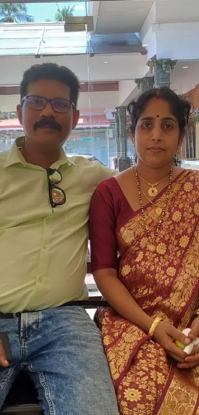 Couple seated indoors, woman in saree and man in casual shirt.