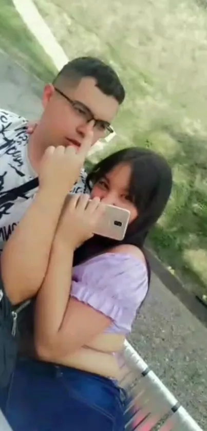 Smiling young couple taking a selfie outdoors on a sunny park bench.