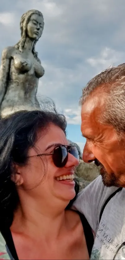 Couple smiling with a sculpture and blue sky.