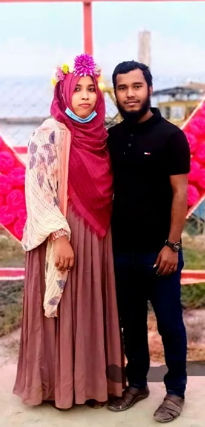 Couple posing in front of heart-shaped pink and red backdrop.